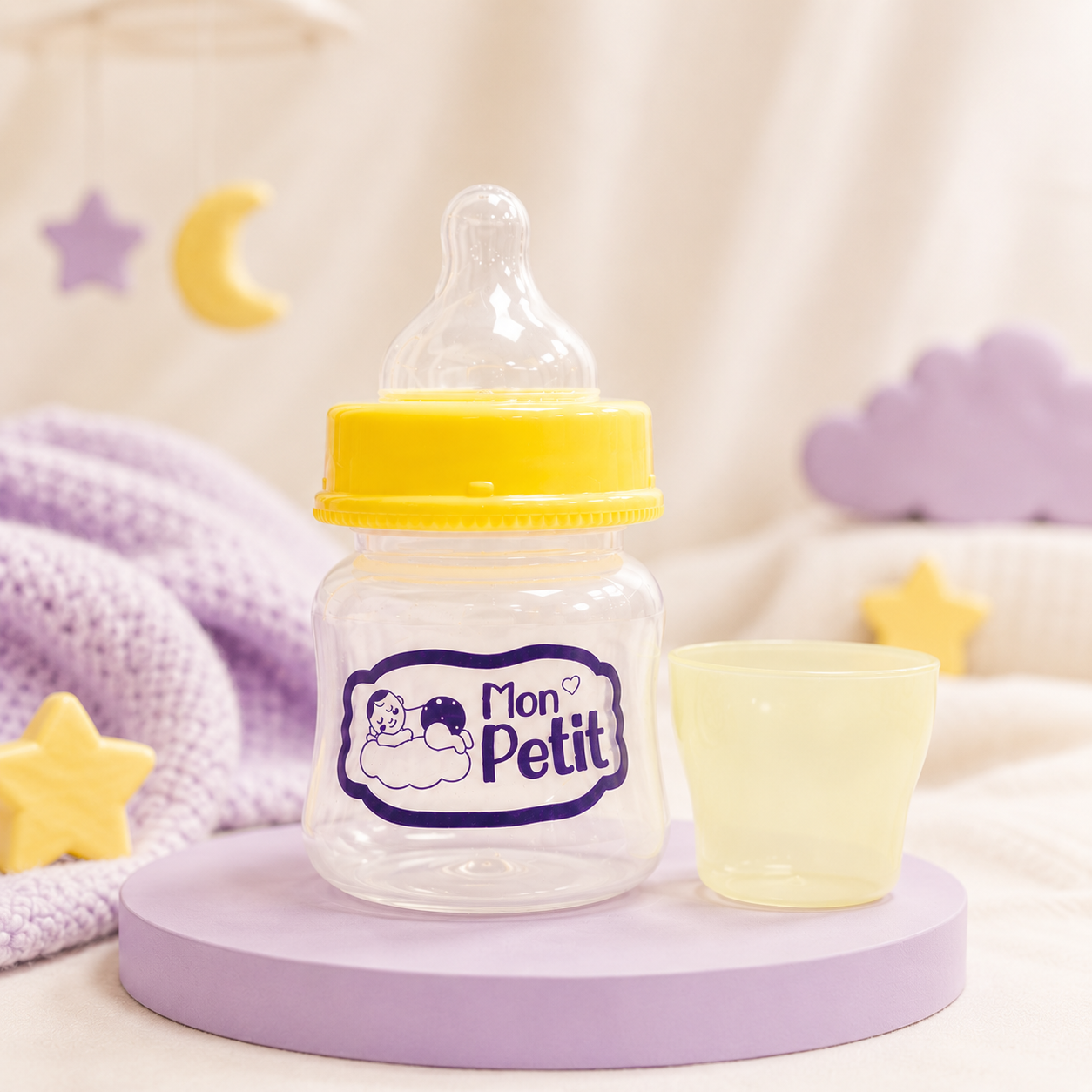 Biberão compacto e copo doseador posicionados num suporte lilás num cenário infantil decorado com estrelas e nuvens.