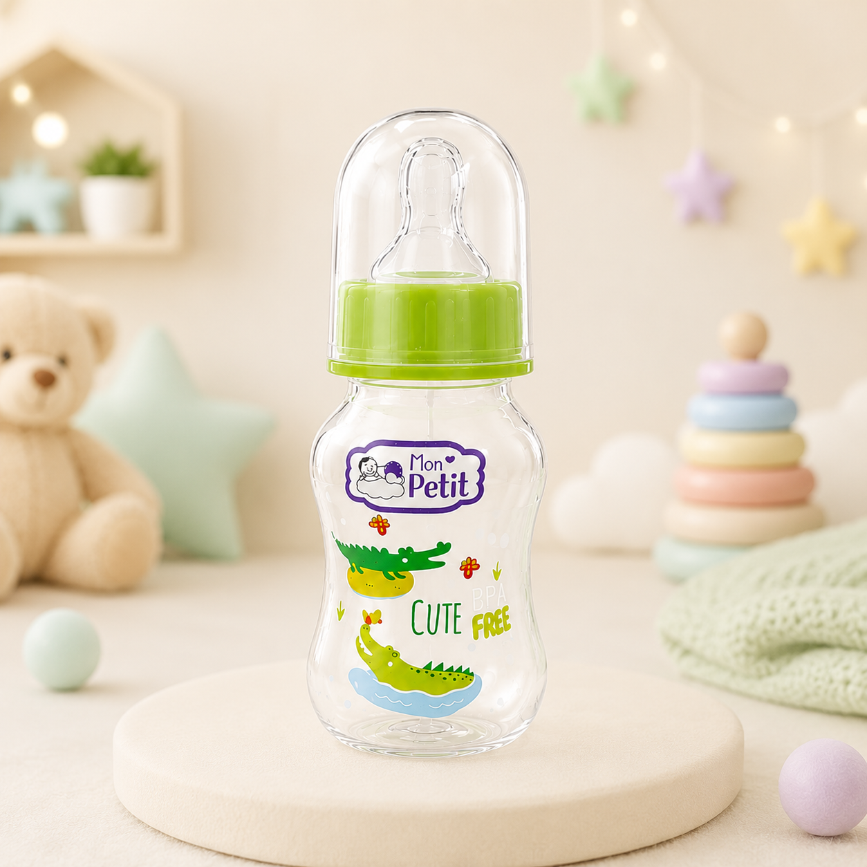 Biberão infantil Mon Petit colocado num suporte redondo decorativo com brinquedos e peluches desfocados ao fundo.