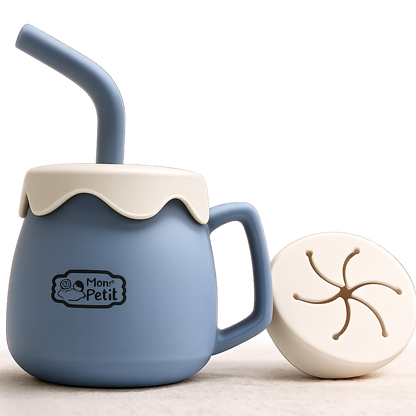 Copo porta-snacks infantil em silicone azul-cinzento com pega lateral, tampa creme estilo onda com palhinha integrada e uma tampa flexível adicional para lanches ao lado.