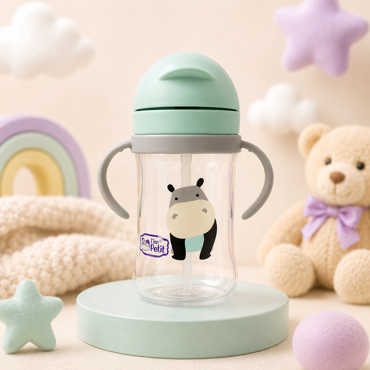 Copo de transição infantil colocado sobre uma base redonda verde-água num quarto decorado com peluche, arco-íris de madeira e estrelas texturizadas.