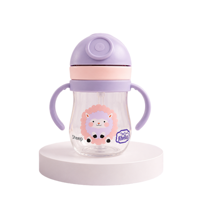 Garrafa infantil de transição transparente com ilustração de uma ovelha lilás e cor-de-rosa, equipada com tampa protetora roxa, faixa rosa e alças ergonómicas, isolada sobre uma base branca.