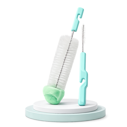 Kit de limpeza infantil contendo uma escova grande com ponta de esponja verde-clara e uma escova fina para bicos, ambas com cabos verde-água, expostas num pódio circular sobre fundo branco.