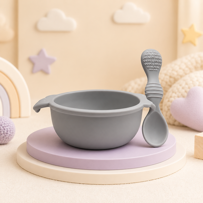 Conjunto de tigela e colher para bebé em silicone cinzento num cenário decorativo infantil.