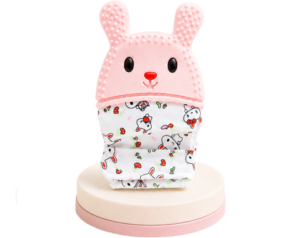 Luva mordedora infantil em formato de coelho rosa com relevos texturizados e base de tecido estampado com pequenos coelhinhos, isolada num suporte circular.
