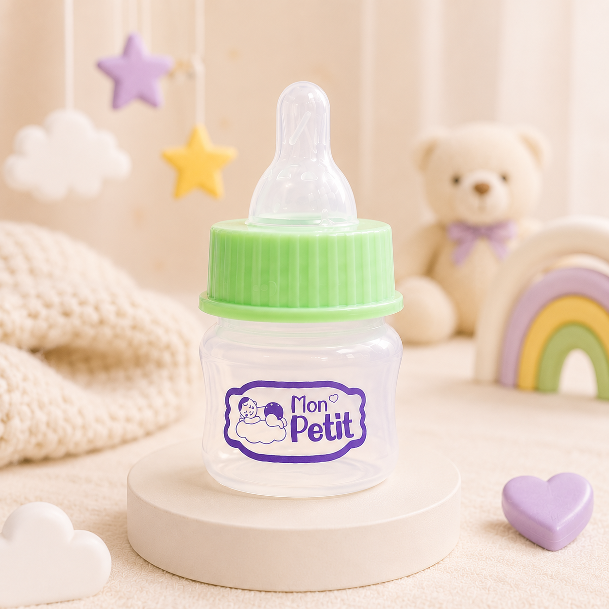 Mini biberão de 50ml posicionado sobre um suporte redondo num quarto de bebé decorado com tons neutros, peluche e arco-íris de madeira.