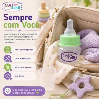 Mini biberão de 50ml acomodado dentro de uma mala de maternidade aberta ao lado de um copo de medição e acessórios de bebé.