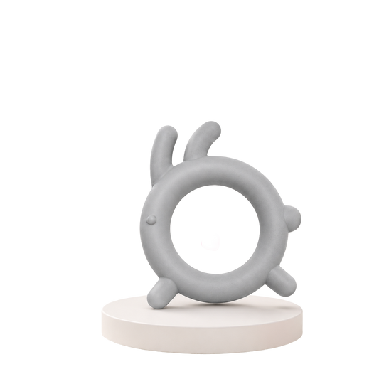 Mordedor sensorial para bebé em silicone macio cinzento com design circular e saliências ergonómicas, posicionado sobre um suporte redondo branco.