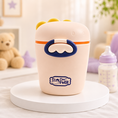 Porta-leite em pó ergonómico posicionado num suporte redondo com um peluche e um biberão desfocados ao fundo.