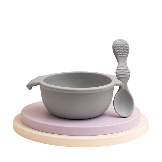 Conjunto de tigela e colher de silicone cinzenta para bebé sobre suporte decorativo.